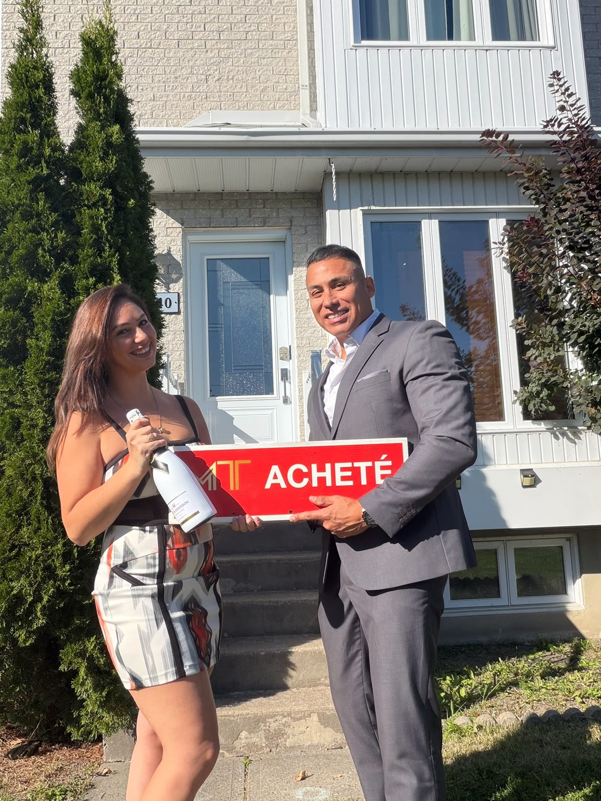 Michael avec une cliente, tenant une pancarte ACHETÉ devant une maison