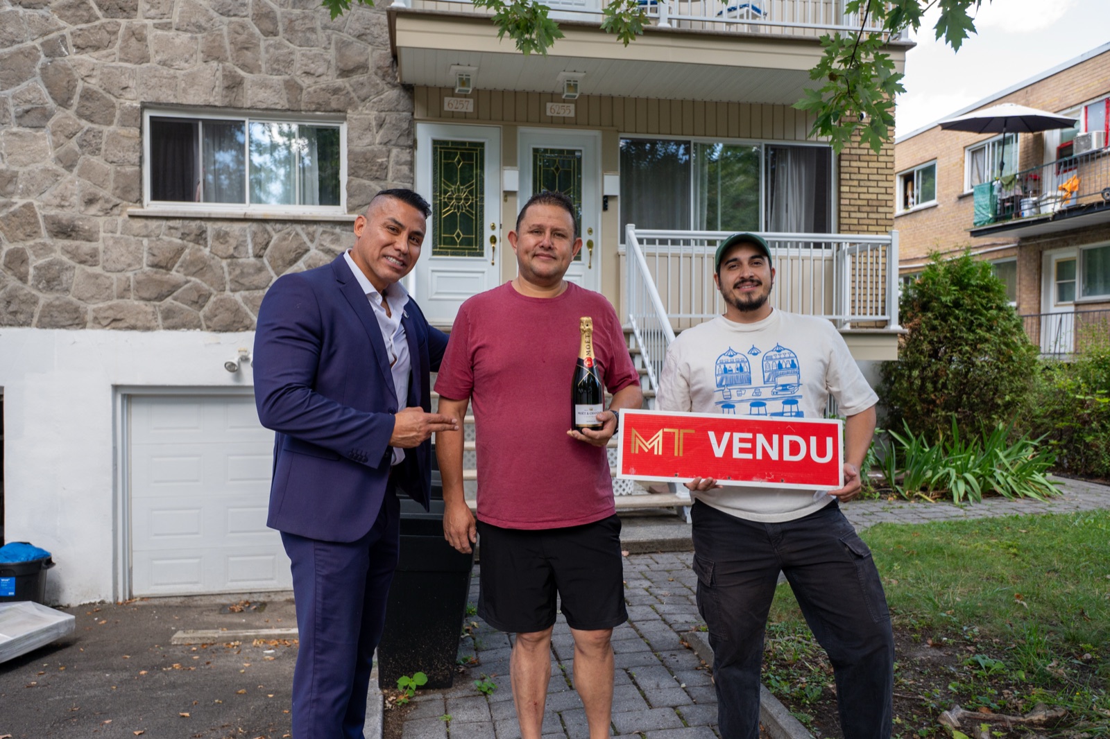 Michael avec deux clients et une pancarte VENDU devant une propriété